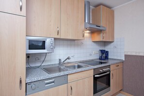 A kitchen with wooden cabinets, a microwave, a sink, a coffee maker, and an oven. - Apartment in Gerolstein-mullenborn (Gerolstein)