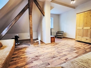 Ein geräumiges Dachzimmer mit Holzdielen, einem großen Kleiderschrank und einem karierten Sessel.