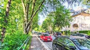 Una calle arbolada con coches aparcados y un edificio con cúpula.