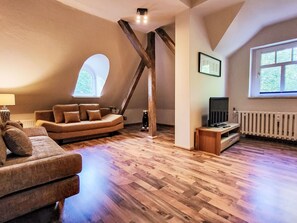 Ein Loft-Zimmer mit Holzboden, einer Couch, einem Fernseher und einem Fenster.