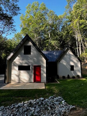 Un bâtiment en bois à deux étages, avec une porte rouge, entouré d’arbres.