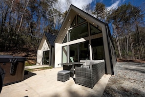 A modern house with large windows, a patio with outdoor furniture, and a garage. - Cozy and Secluded Cottage in the Woods of Western North Carolina, near Pisgah National Forest (Balsam Grove)