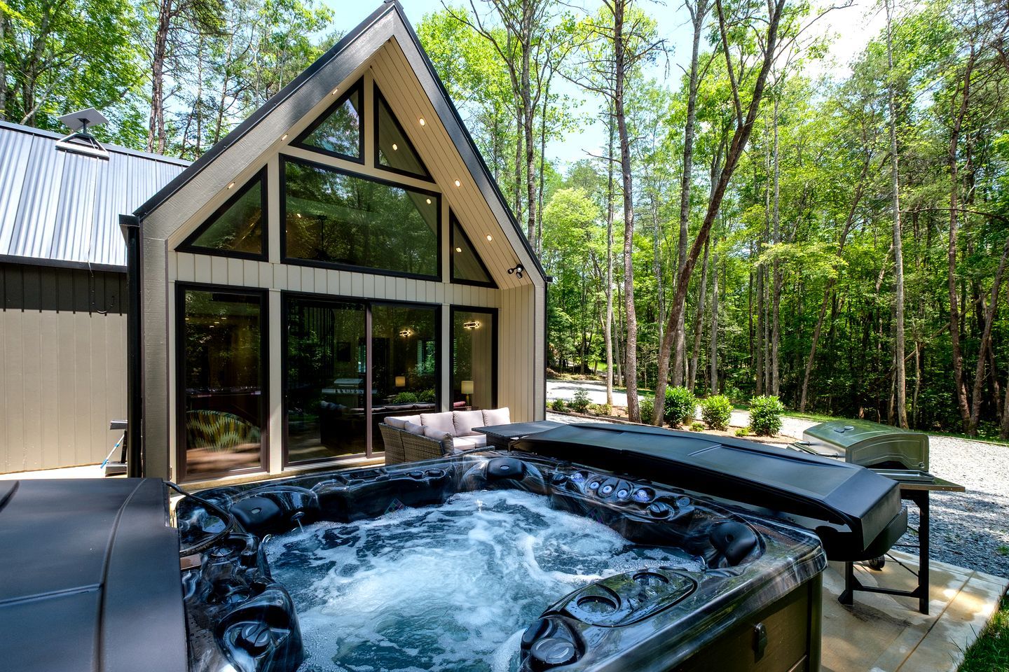 A modern house with a hot tub, large windows, and a forested backdrop.
