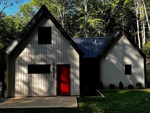Un immeuble de deux étages avec une porte rouge et une petite fenêtre à l’étage supérieur.