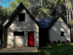 A two-story building with a red door and a small window on the upper floor. - Cozy and Secluded Cottage in the Woods of Western North Carolina, near Pisgah National Forest (Balsam Grove)