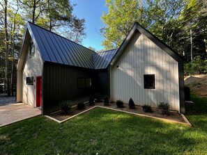 Un bâtiment moderne doté d’un toit en pente, d’une porte rouge et d’un petit jardin agrémenté d’arbustes.
