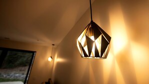 Een geometrische hanglamp in een kamer met een raam en een wandlamp.