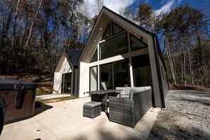 Une maison moderne dotée de grandes fenêtres, d’un patio avec mobilier d’extérieur et d’un garage.