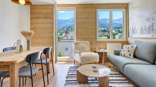 A modern living room with a wooden floor, a round coffee table, a grey sofa, a fluffy chair, and a dining table with chairs.
