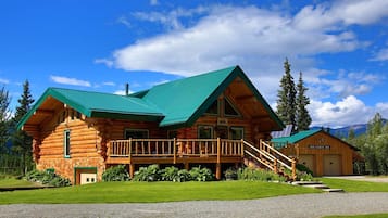 A log cabin with a green roof, a porch, and a garage.