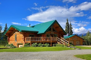 A log cabin with a green roof, a porch, and a garage.