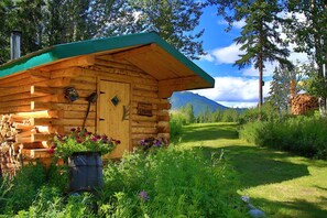 A wooden cabin with a green roof, a sign reading 'SAUNA,' and a log pile outside.