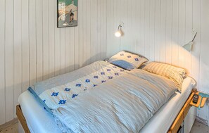 Ein Einzelbett mit gemustertem Bettbezug, eine Wandlampe und ein gerahmtes Bild.