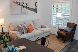 A living room with a sofa, armchair, dining table, lamp, and artwork on the wall. - Creek Cabin ADA accessible in Livingston, Texas (Livingston)