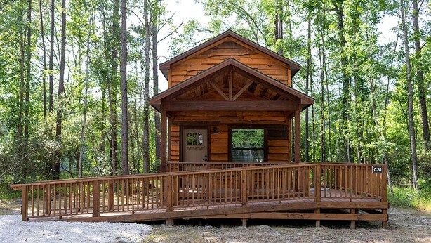 A wooden cabin with a porch and a door, surrounded by trees. - Creek Cabin ADA accessible in Livingston, Texas (Livingston)