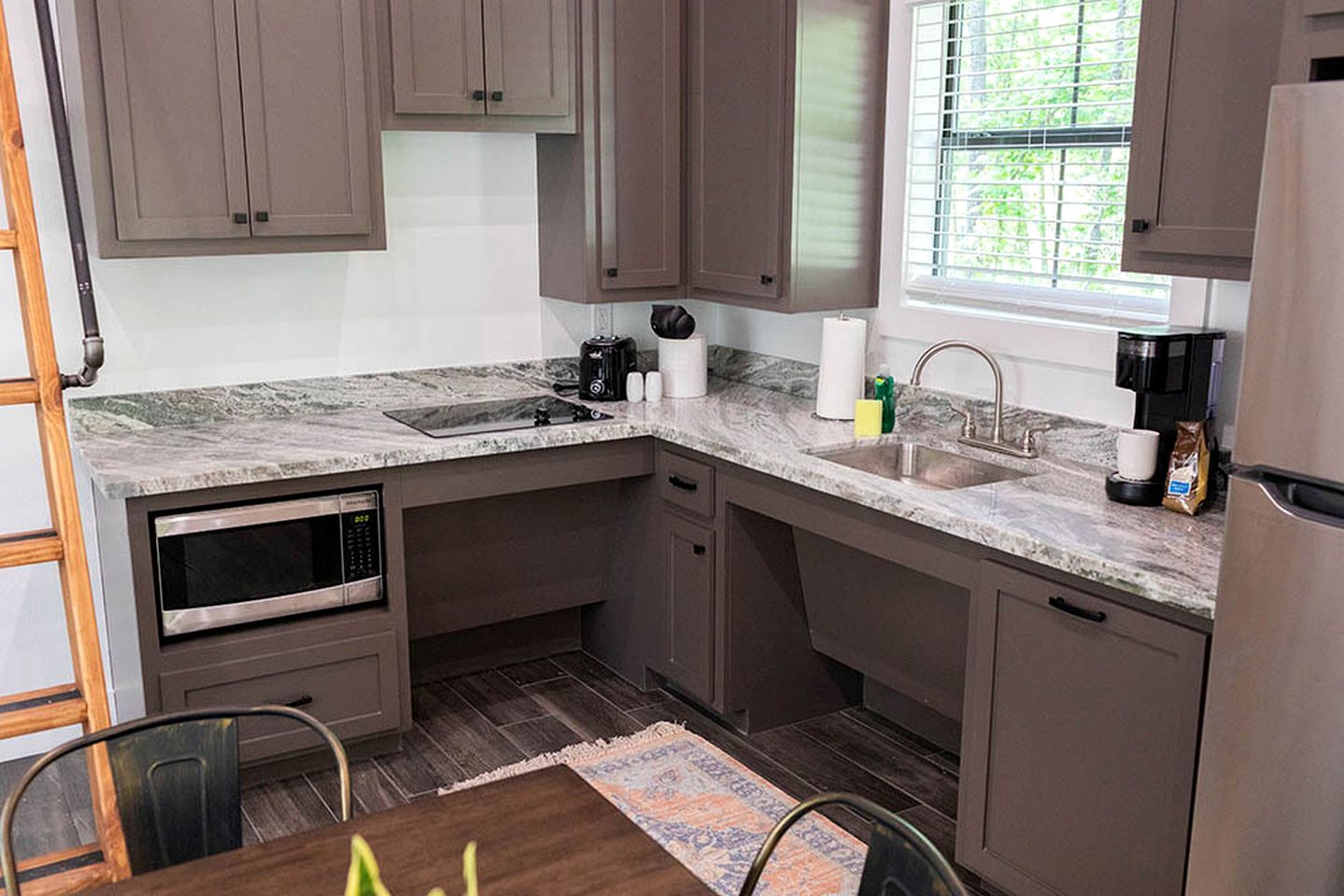 A kitchen with a built-in oven, a sink, and a window with blinds.