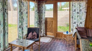 Una habitación acogedora con una silla de madera, una mesita, un sofá y vistas al exterior a través de amplias ventanas.