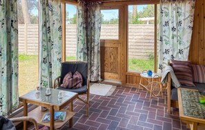 A cozy room with a wooden chair, a small table, a sofa, and a view of the outdoors through large windows. - 2 bedroom cozy home in Store Fuglede (Store Fuglede)