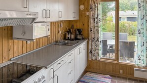 Cocina compacta con microondas, estufa y pileta, paneles de madera y vista al exterior.