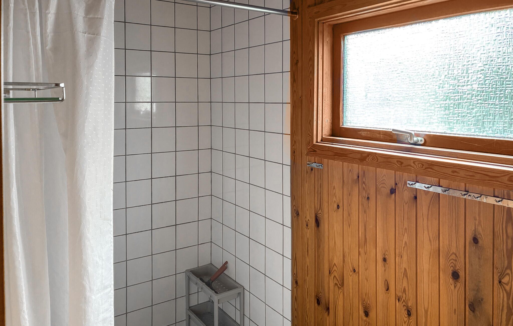 A bathroom with white tiles, a wooden door with a window, and a shower curtain.