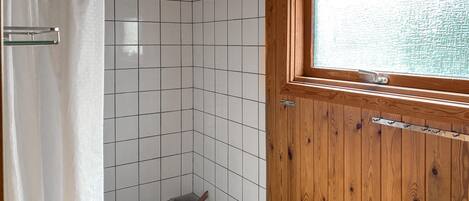 A bathroom with white tiles, a wooden door with a window, and a shower curtain.