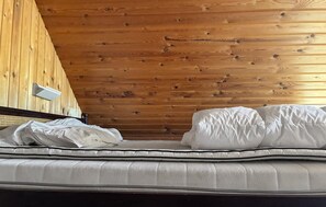 Ein Einzelbett mit weißer Bettwäsche in einem Raum mit holzverkleideter Decke.