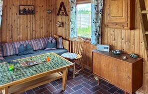A cozy cabin interior with a wooden wall, a sofa, a dining table, a chair, a cabinet, and a window with curtains. - 2 bedroom cozy home in Store Fuglede (Store Fuglede)