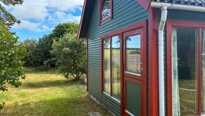 Una casa con fachada verde y detalles en rojo, una ventana visible y un jardín cubierto de césped.