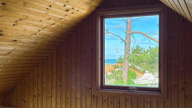 Interior de madera con una ventana que da a un árbol y un edificio.