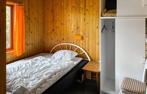 A single bed with a white mattress and pillows, a wooden nightstand, a small table, and a white wardrobe with a mirror. - 2 bedroom cozy home in Store Fuglede (Store Fuglede)