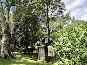 Ein kleines, eingeschossiges Haus mit Satteldach, umgeben von dichten Bäumen und einem Rasen.