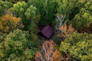An aerial view of a forested area with a single building featuring a red roof. - Romantic 1-Bedroom Cabin with Fireplace, Hot Tub & Nature Views Near Broken Bow (Broken Bow)