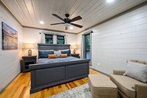 A bedroom with a bed, bedside tables, a ceiling fan, and a window. - Romantic 1-Bedroom Cabin with Fireplace, Hot Tub & Nature Views Near Broken Bow (Broken Bow)