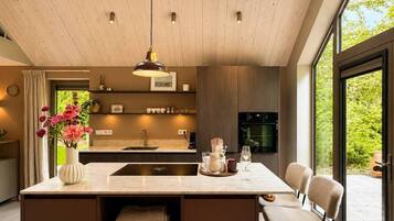 Una cocina moderna con una isla central, iluminación colgante y vista a espacios verdes.