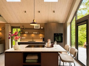 Una cocina moderna con una isla central, iluminación colgante y vista a espacios verdes.