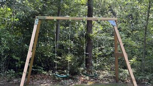 A wooden swing set in a grassy area with trees in the background. - Holiday home Koningsbos – At home in the forest (Emst)