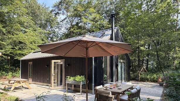 A rustic cabin with a patio, wooden furniture, and a large umbrella. - Holiday home Koningsbos – At home in the forest (Emst)