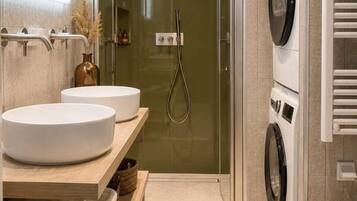 Een moderne badkamer met twee wastafels, een douche, een wasmachine en een toilet.