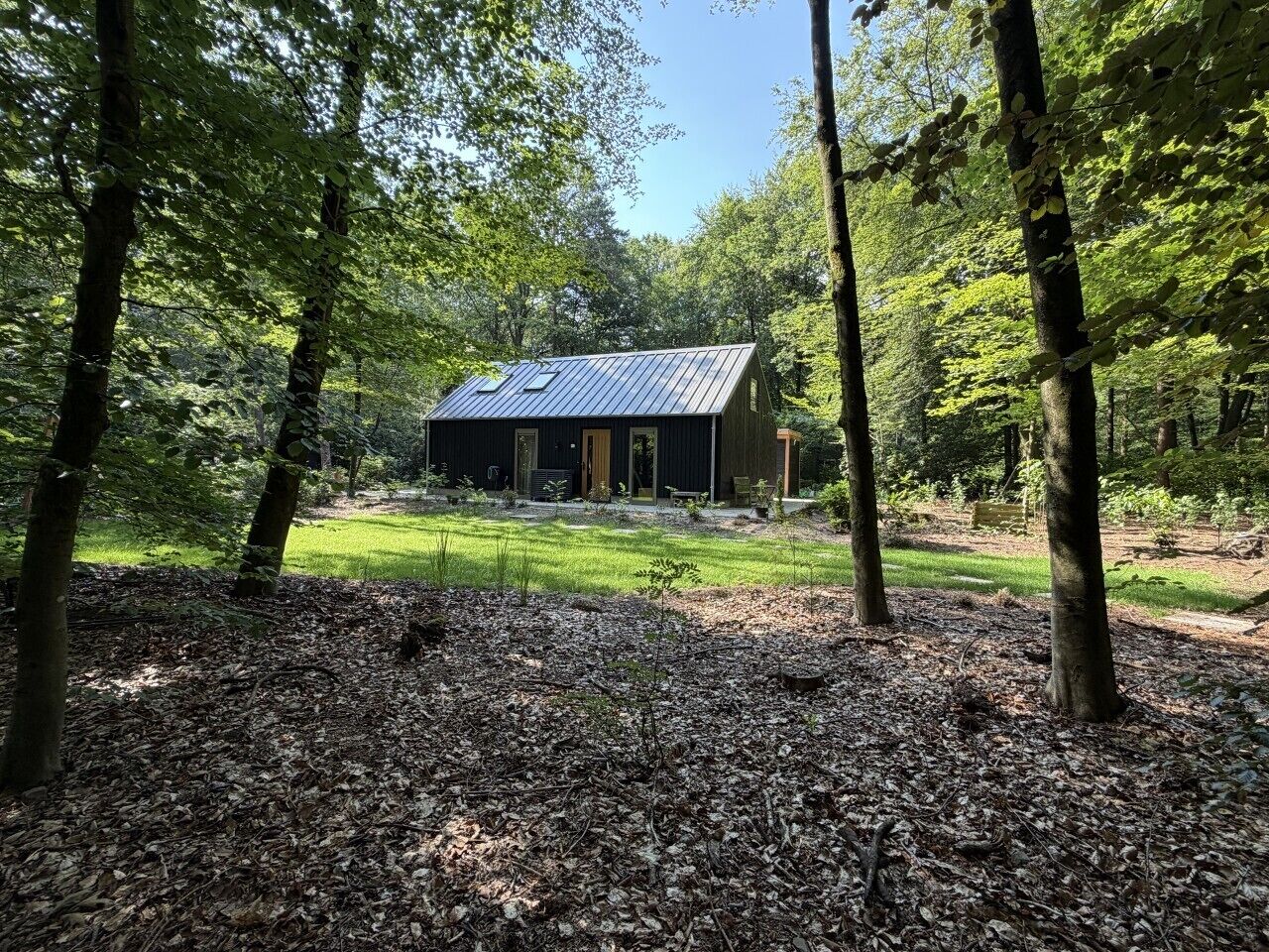 Una cabana amb teulada metàl·lica, envoltada d'arbres i una zona verda.