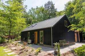 Een klein, donker gebouw met schuine dak en een enkele deur, en een klein portaal met een bankje.