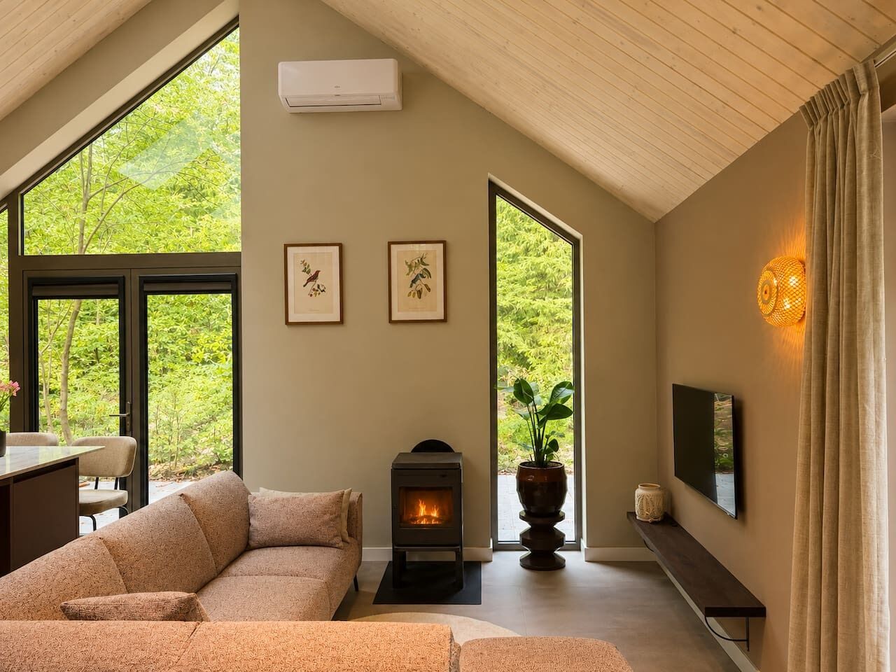 Un salon moderne avec un canapé, une cheminée, un téléviseur et une grande fenêtre donnant sur un paysage verdoyant.