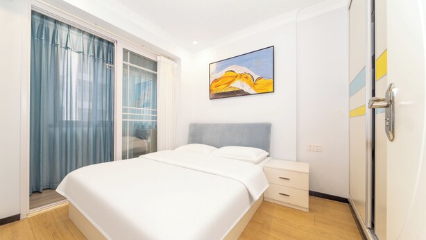 Um quarto com cama, mesa de cabeceira, guarda-roupa, janela com cortinas e um quadro na parede.