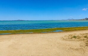 Ein Strand mit klarem, blauem Wasser, sandigem Ufer und fernen Bergen.
