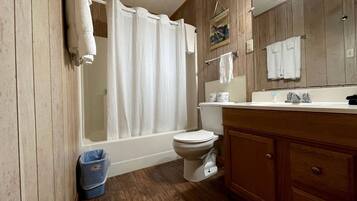 A bathroom with a bathtub, toilet, wooden vanity, and a mirror.