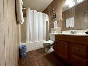 A bathroom with a bathtub, toilet, wooden vanity, and a mirror. - Inviting Lakefront Cabin with Boat Launch near Zwolle, Louisiana (Zwolle)