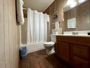 A bathroom with a bathtub, toilet, wooden vanity, and a mirror. - Inviting Lakefront Cabin with Boat Launch near Zwolle, Louisiana (Zwolle)