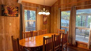 A wooden dining room with a large table and chairs, a chandelier, and large windows with curtains.