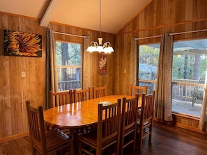 A wooden dining room with a large table and chairs, a chandelier, and large windows with curtains. - Inviting Lakefront Cabin with Boat Launch near Zwolle, Louisiana (Zwolle)