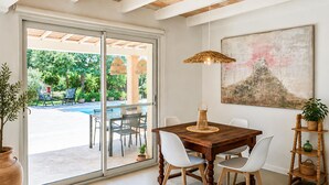 Un comedor con una mesa y sillas de madera, una lámpara colgante y un cuadro grande en la pared.