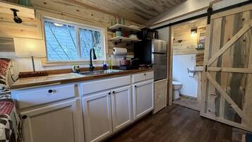 A wooden cabin interior with a kitchen, white cabinets, a wooden floor, and a sliding barn door.